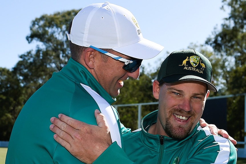 Two men hug while wearing Australia cricket gear.