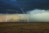 Lightning strikes under a dark cloud across a bare landscape