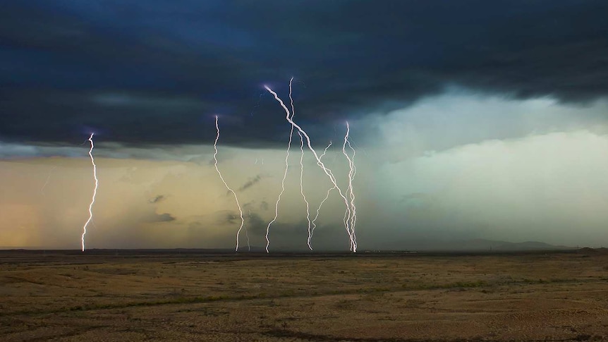 Lightning strikes under a dark cloud across a bare landscape