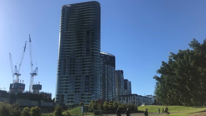 Opal Tower, a tall residential building surrounded by other apartments and a construction site, backing on to green parkland.
