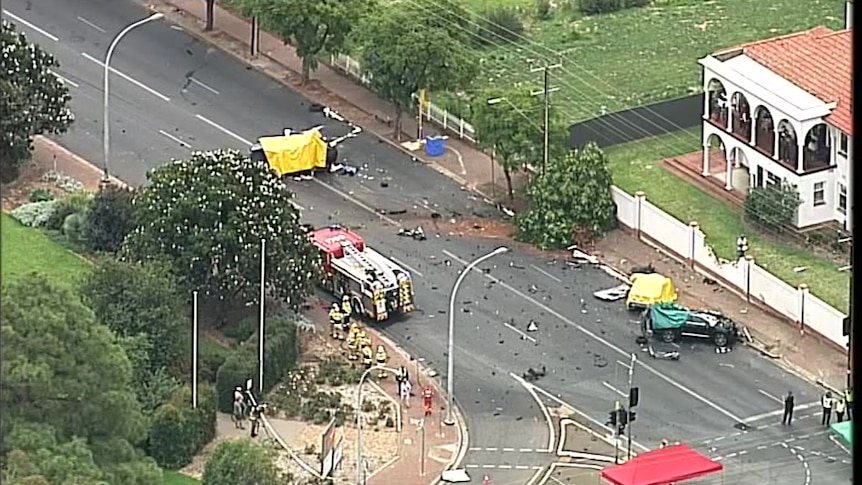 A birds-eye view of a crash scene involving three cars. Debris can be seen strewn across the road.