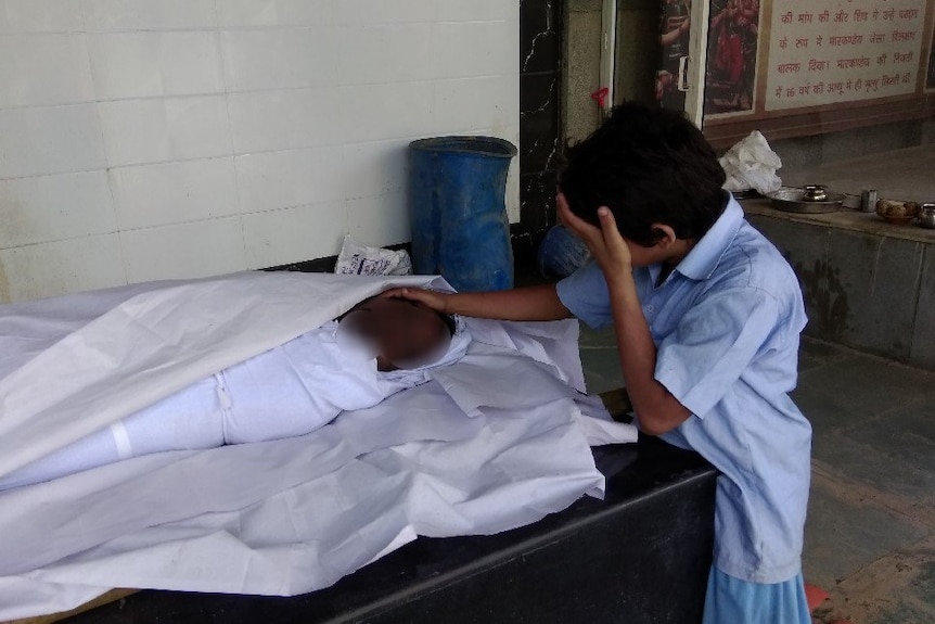 A sad-looking boy puts his hand on the head of his dead father.