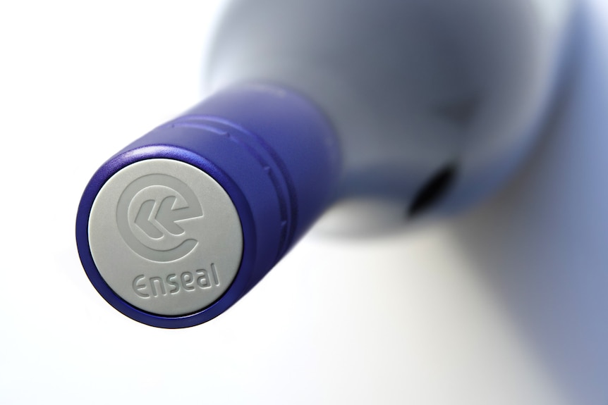 A close-up of a wine bottle screw top grey and blue cap with enseal and a symbol engraved on top.
