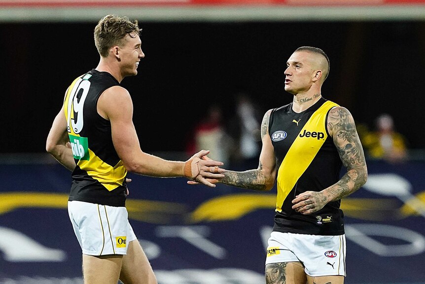 Two Richmond AFL players touch hands as they celebrate a goal against the Western Bulldogs on the Gold Coast.
