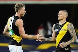 Two Richmond AFL players touch hands as they celebrate a goal against the Western Bulldogs on the Gold Coast.