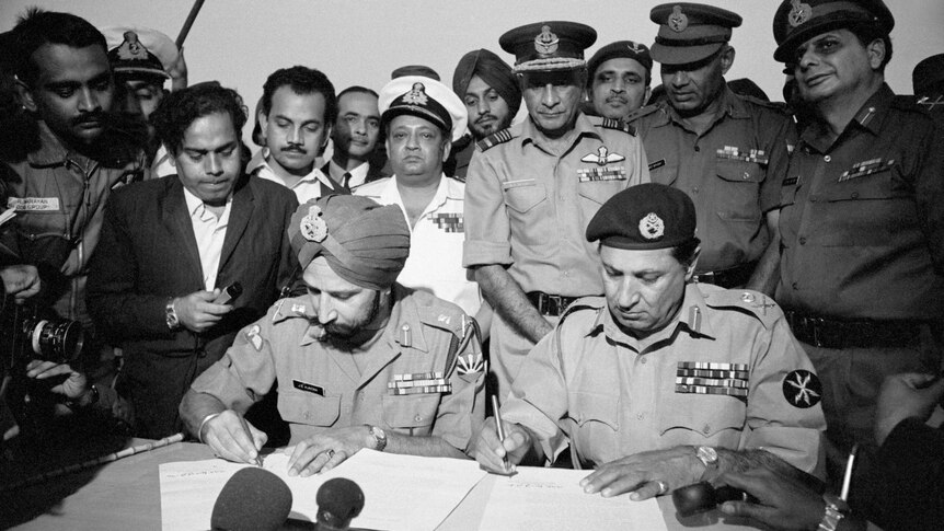 Military leaders of India and Pakistan, surrounded by onlookers, sign the peace treaty that ended the war between them in 1971.