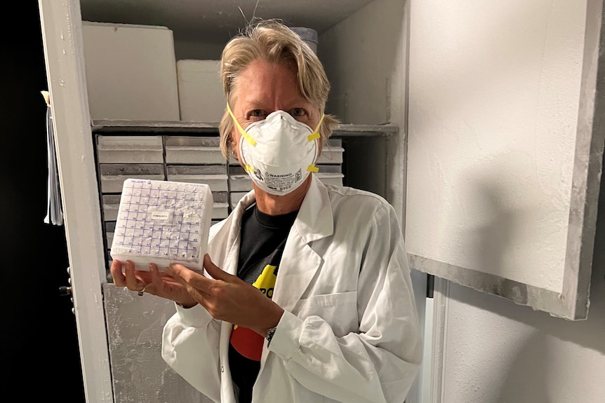 Woman in white coat holding a small plastic container 