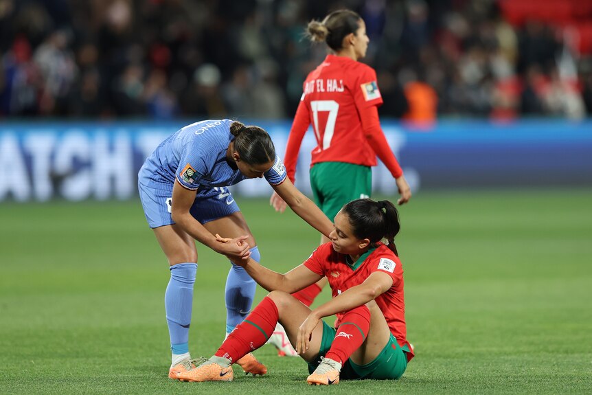 Estelle Cascarino of France helps Sakina Ouzraoui of Morocco off the ground at the FIFA Women's World Cup.