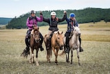Three tired riders astride small Mongolian ponies with hands upraised in victory