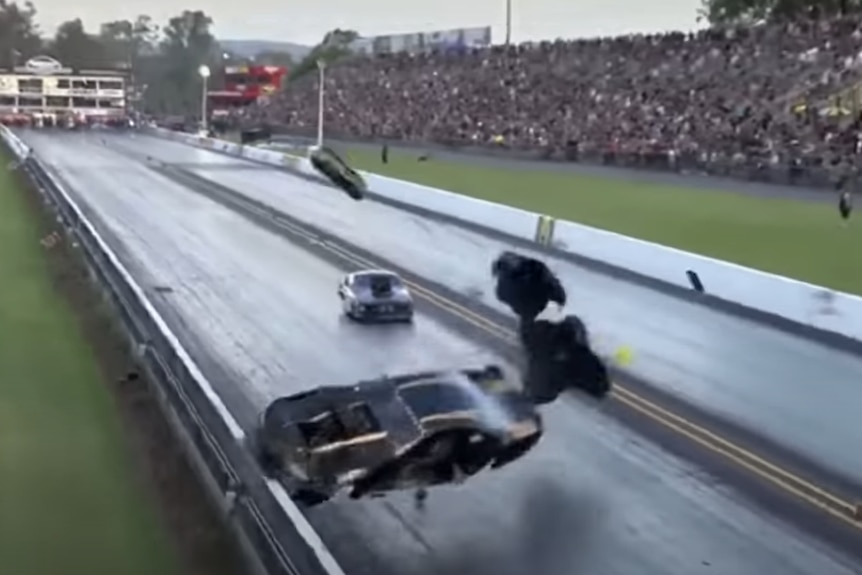 A black and gold car careens off the side of a drag racing track as fans look on from nearby stands.