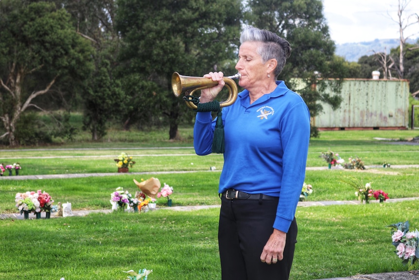 A person plays the Last Post on a bugle. 