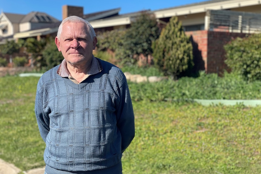 An elderly man standing in a grassy front yard