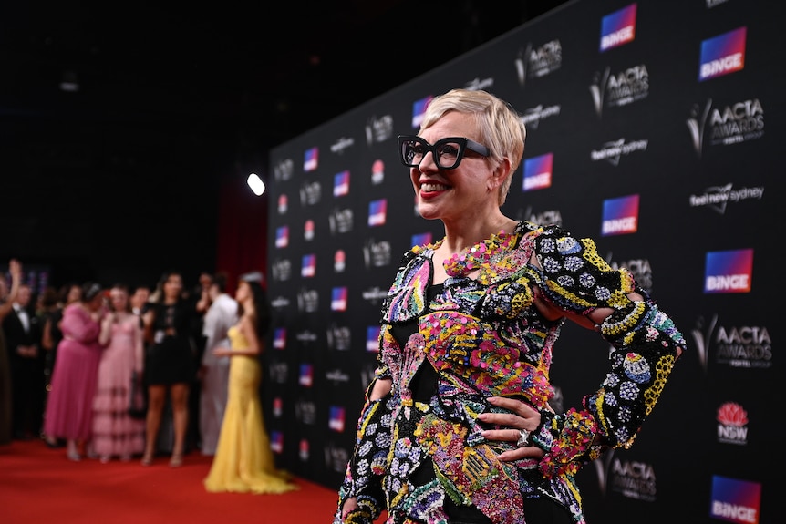 Catherine Martin, a middle-aged white woman with short blonde hair, wears thick glasses and a colourful beaded dress.