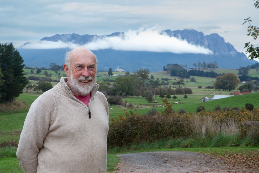 A man smiles to camera with the long, loaf shape of Mt Roland in the background.