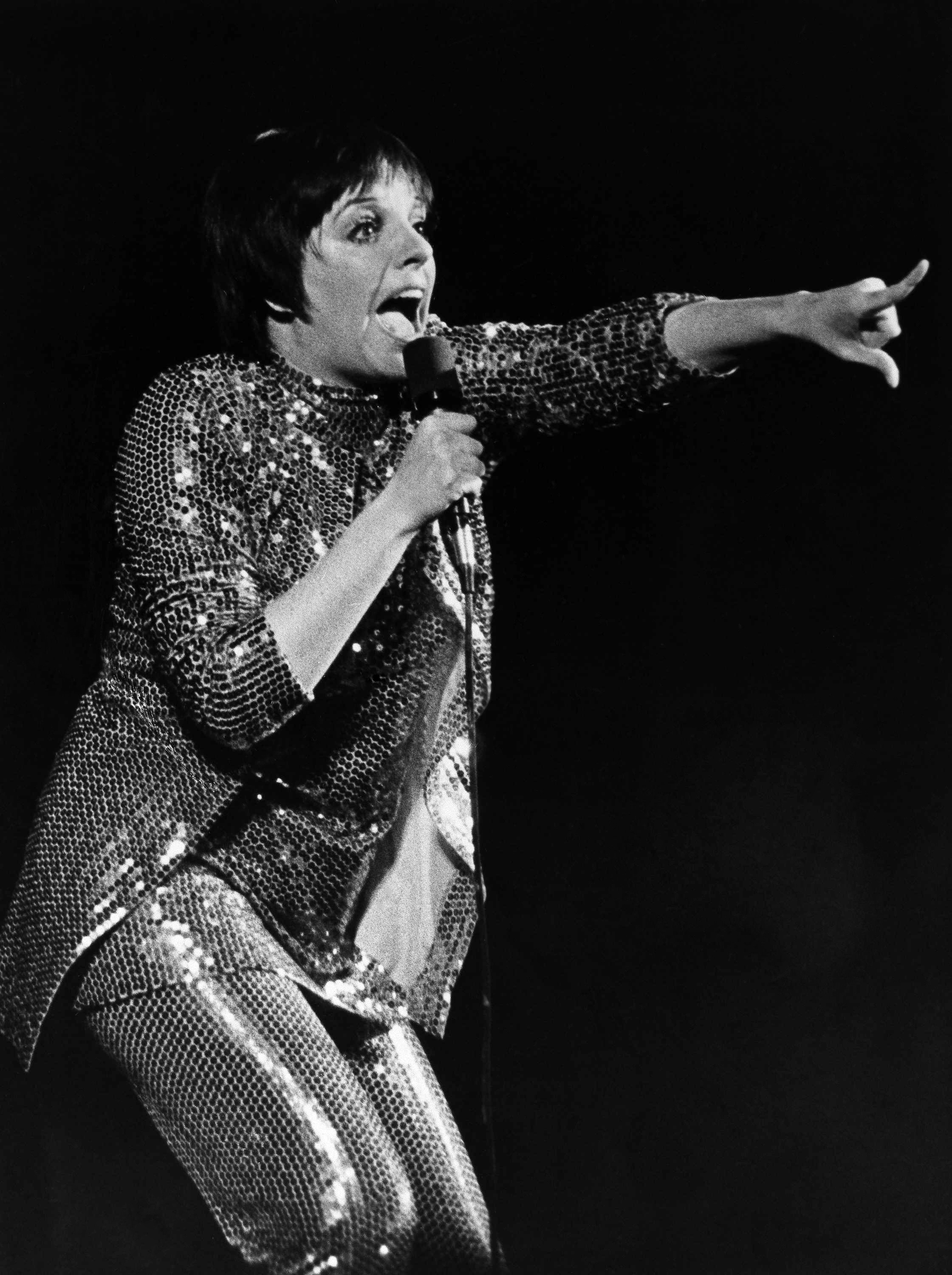 A black and white photo of Liza Minelli in a sequinned outfit performing on stage in 1975.