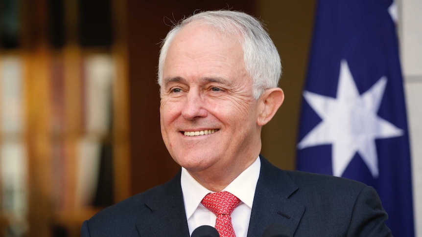 Malcolm Turnbull smiles as he stands in front of microphones.