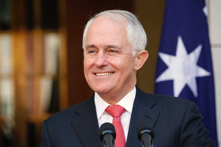 Malcolm Turnbull smiles as he stands in front of microphones.