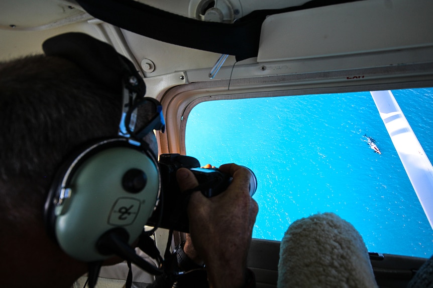 A man in black clothing photographs a while through the window of a plane