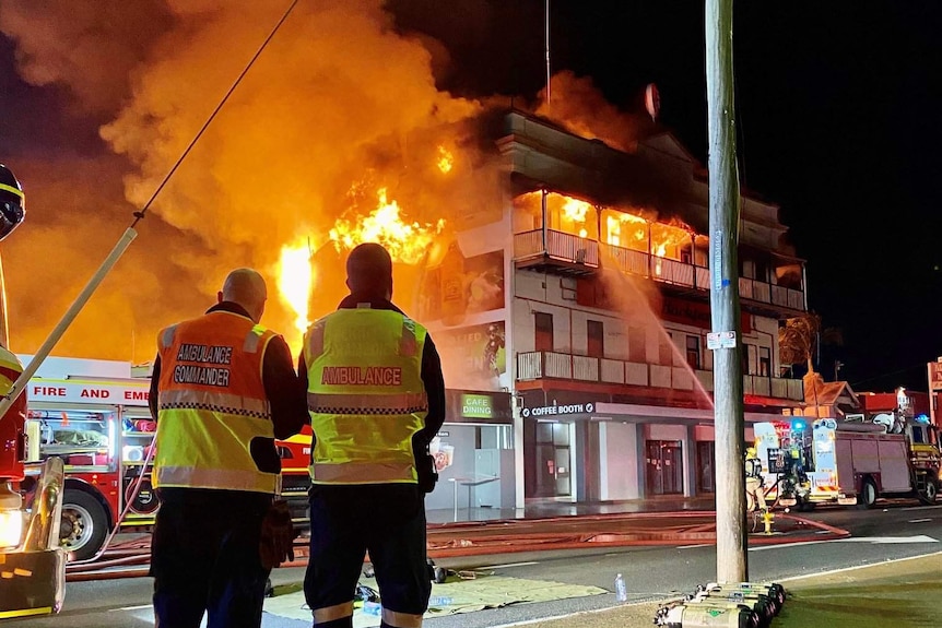 Two fire fighters stand in front of a building on fire