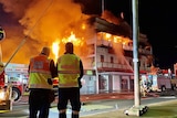 Two fire fighters stand in front of a building on fire