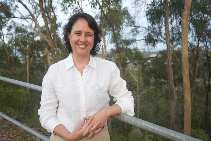 a woman smiles in front of some trees