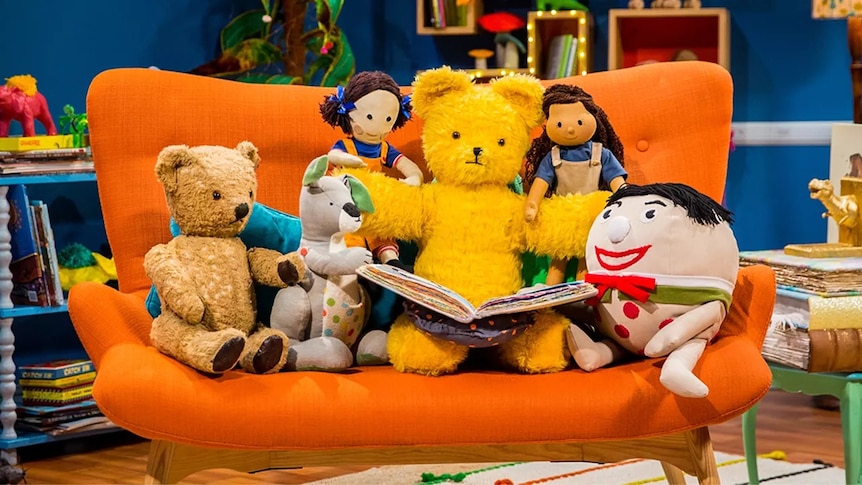 Play School toys sitting on a couch reading a book