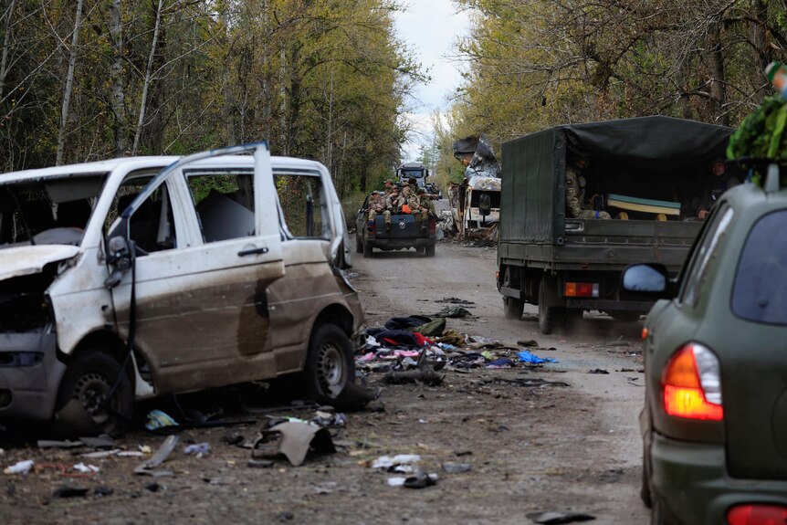 Ukrainian army soldiers drive past a blasted white van.