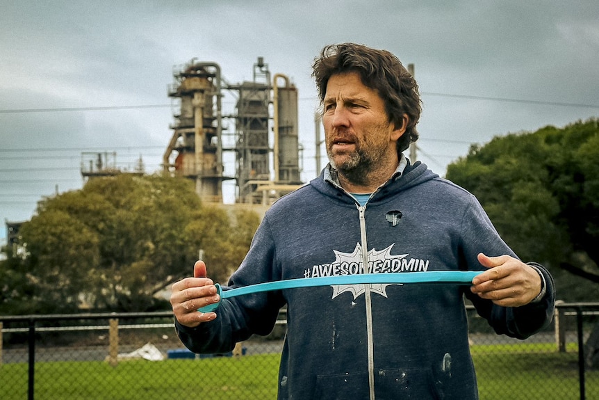A man in a park in front of a refinery.