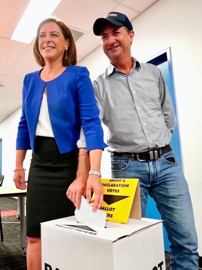 A woman and a man smile as they put their voting ballot in a box.