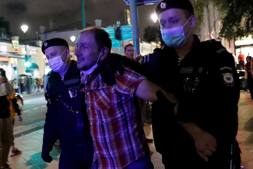 Two police wearing masks hold a man wearing red check shirt