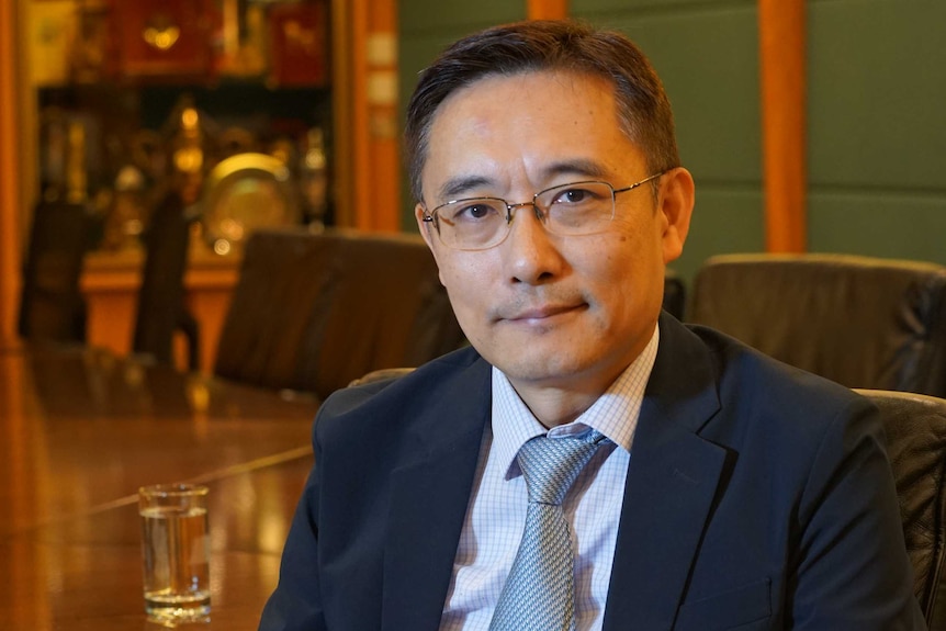 A Chinese man in a suit sitting in a wooden boardroom