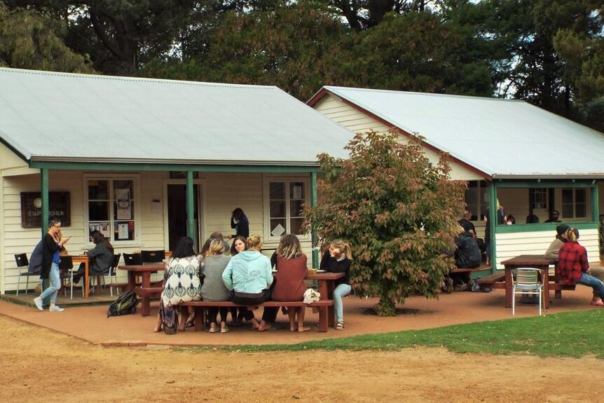 People gather on outdoor benches next to two huts serving food