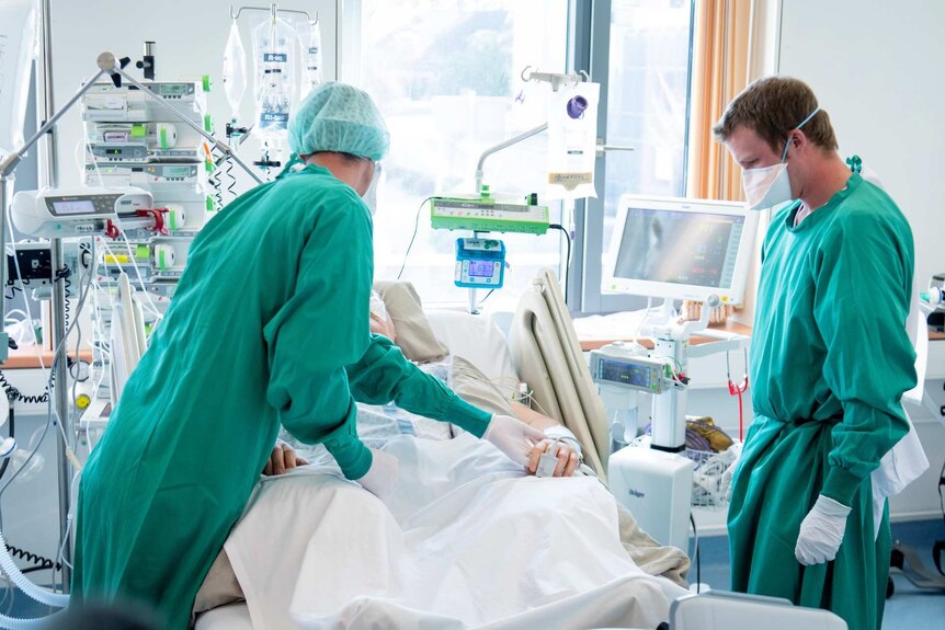 Two medical workers stand over a COVID-19 patient lying in a hospital bed.