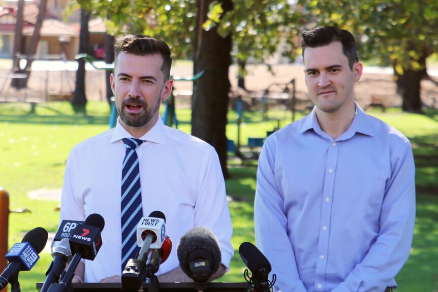 Two men in business shirts hold a press conference in a park