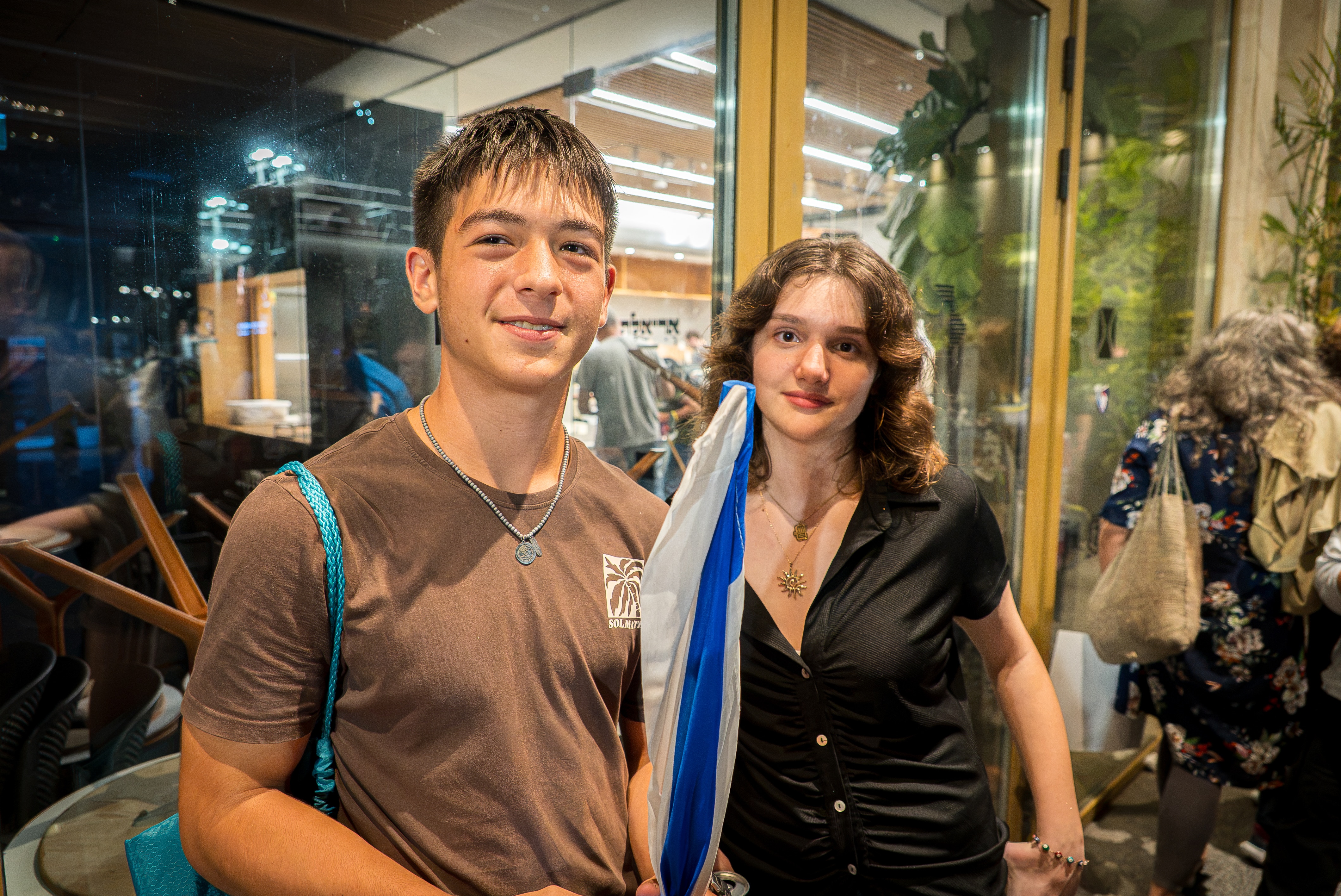 Tomer (left) and Zoya stand outside and talk to the ABC, holding a blue and white flag.