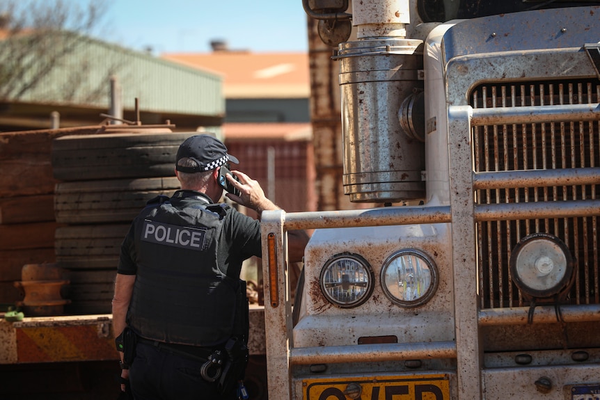 Un policier s'appuie contre un camion tout en parlant sur un téléphone portable. 