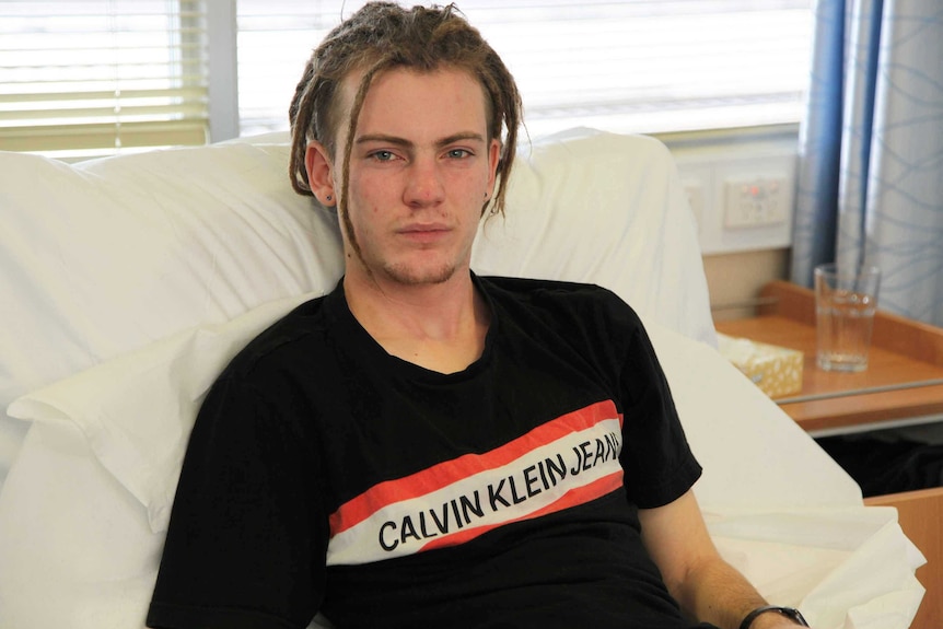 20-year-old Benjamin Bruce sits on a hospital bed wearing jeans and a t-shirt.
