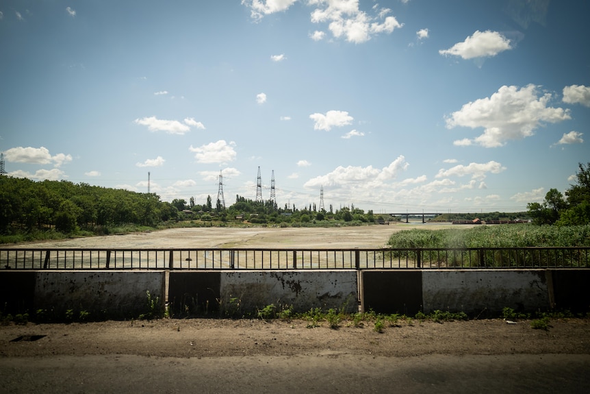 A dry river bed is seen from a dusty bridge. Electricity poles dot the horizon in the distance