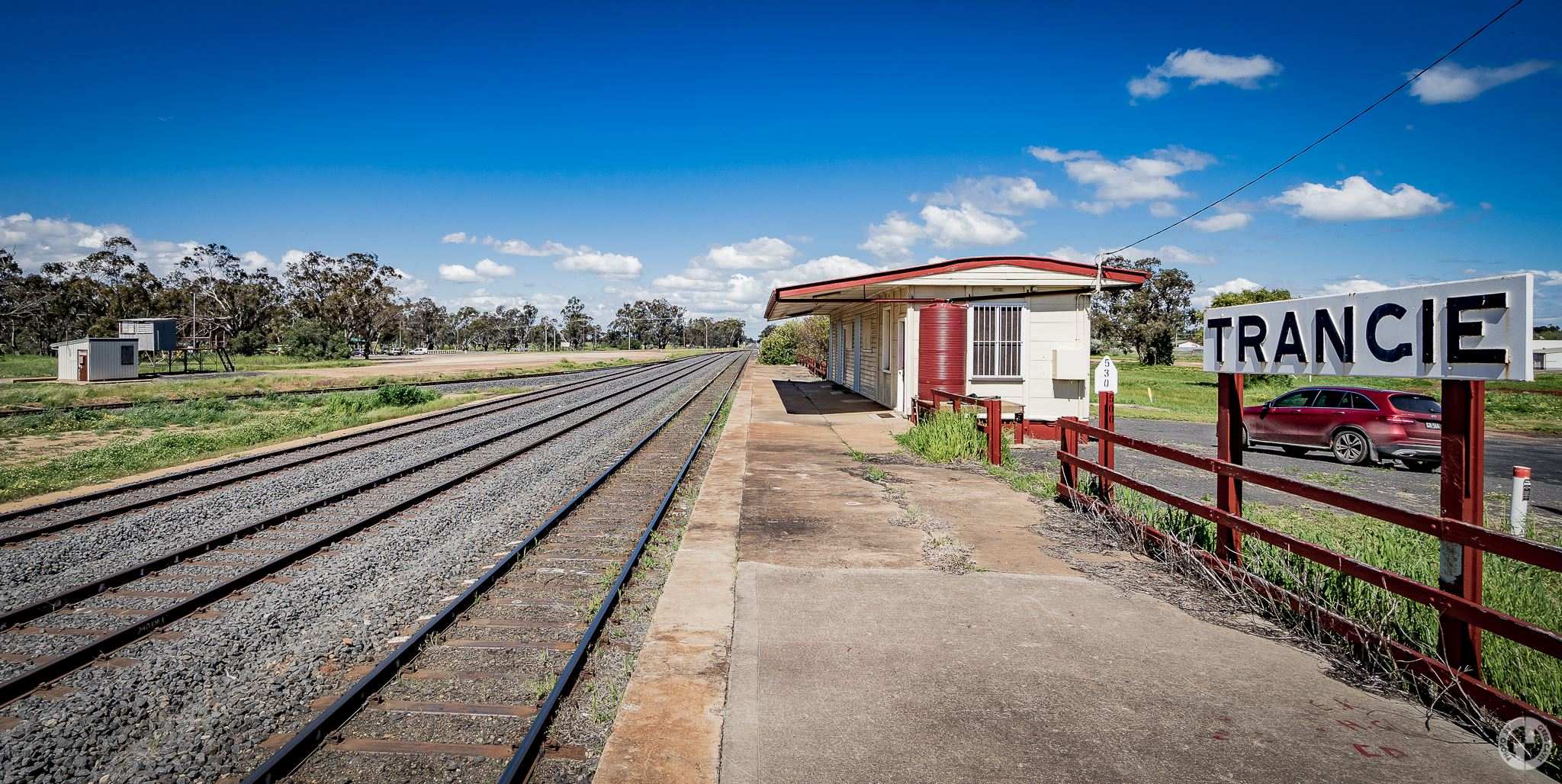 Railway lines on the left and small railway station and red car on the right