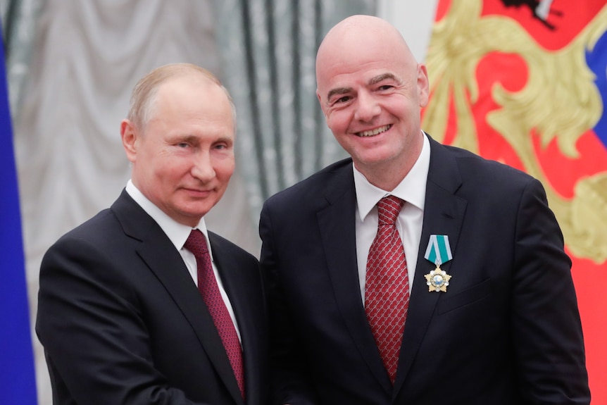 Russian President Vladimir Putin shakes the hand of FIFA president Gianni Infantino after pinning a medal on his chest.
