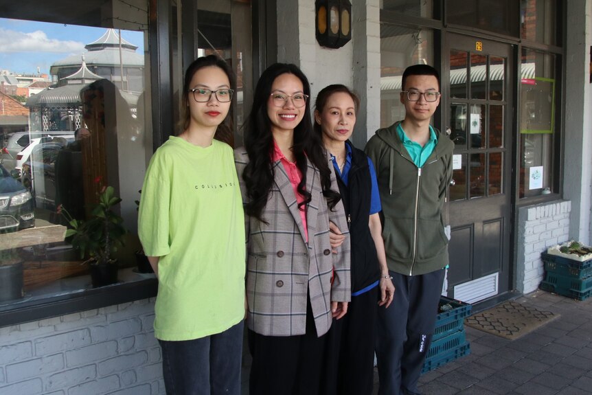 A Vietnamese family of four stand outside a restaurant with big smiles on their faces.