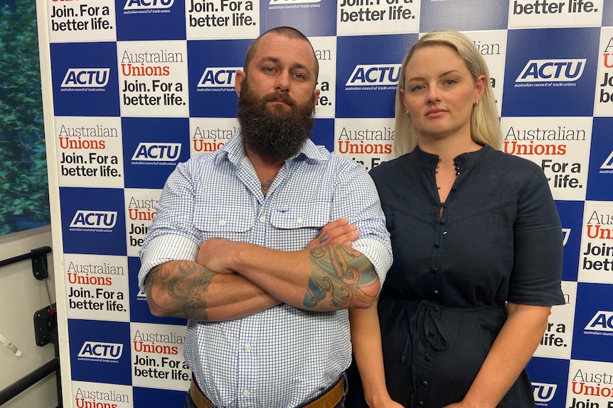 Kyle and Jo stand in front of an ACTU sign, looking serious.