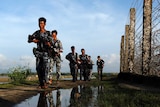 Myanmar police officers patrol along the border fence carrying guns.