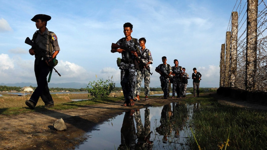 Myanmar police officers patrol along the border fence carrying guns.