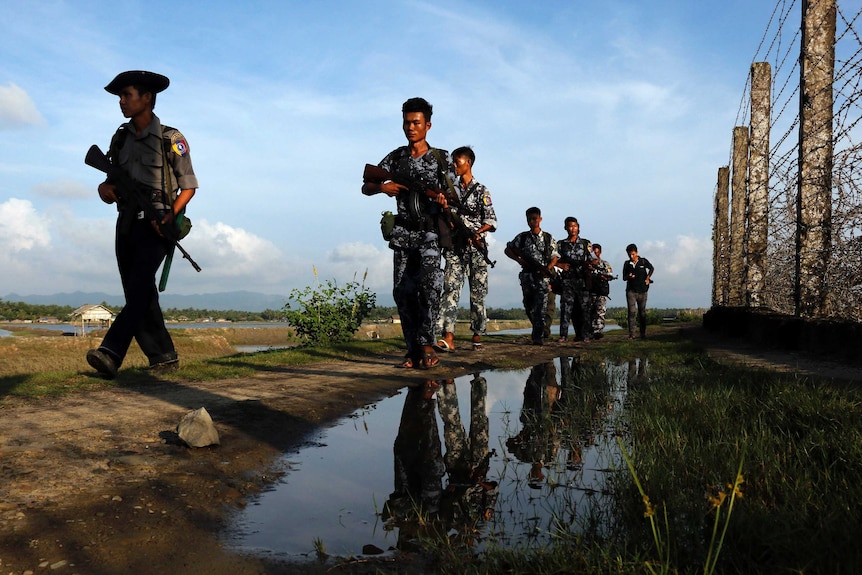 Myanmar police officers patrol along the border fence carrying guns.