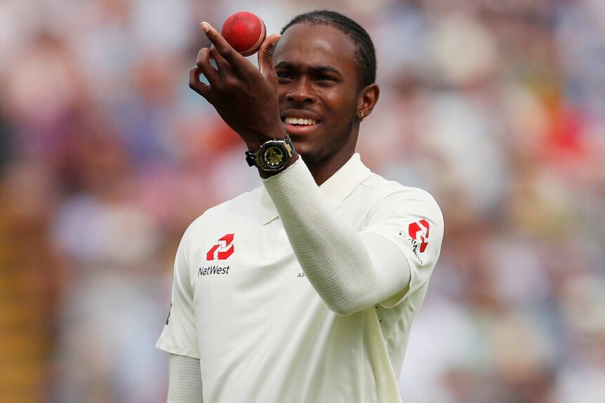 A bowler inspects the cricket ball while holding it between his thumb and forefinger.