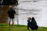 A man, woman and young child look out at a flooded river.