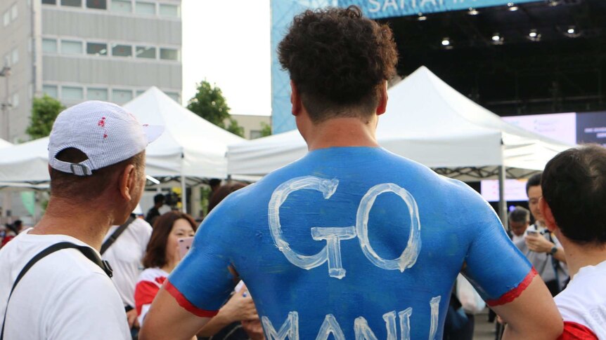 A male Japanese rugby union supporter wearing body painted samoa jersey with "Go Manu" written on his back.