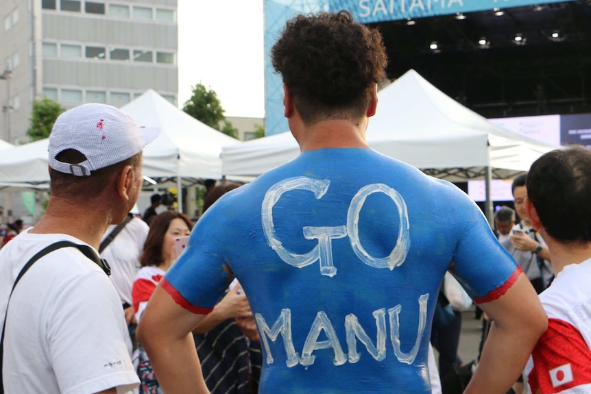 A male Japanese rugby union supporter wearing body painted samoa jersey with "Go Manu" written on his back.