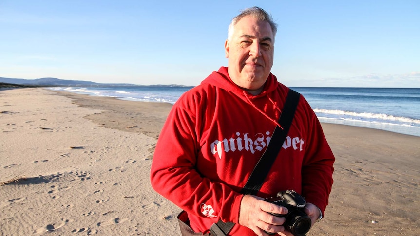A photographer wearing a red jumper stands on a beach